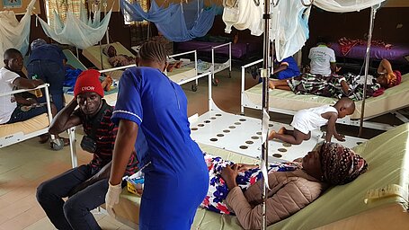 Die Krankenstation in der Gesundheitsklinik in Jaiama, Sierra Leone. Viele offene, belegte Betten mit Mückenschutz in einem großen Raum.
