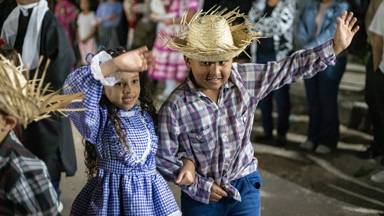 Zwei brasilianische Kinder tanzen und winken. Sie sind als brasilianisches Farmerpaar verkleidet.